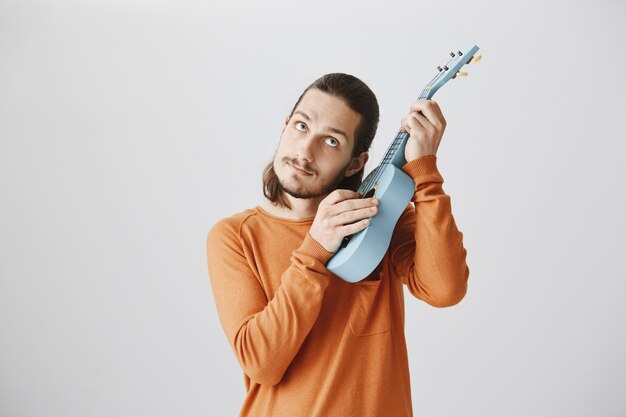 Ragazzo carino hipster intona le corde, suonando l'ukulele