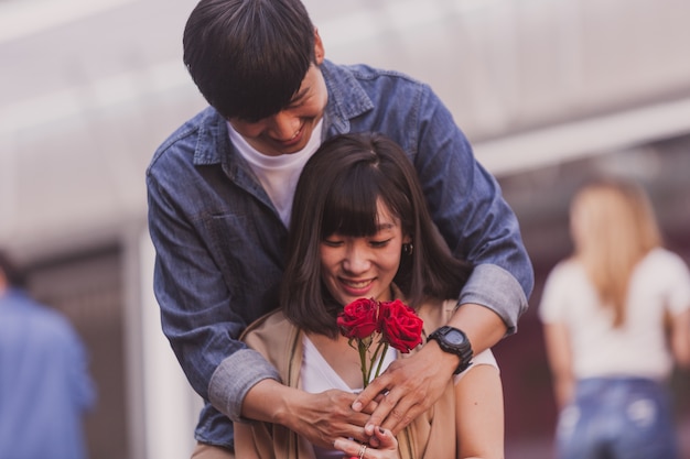 Ragazzo che abbraccia dietro la sua ragazza e dando le sue rose