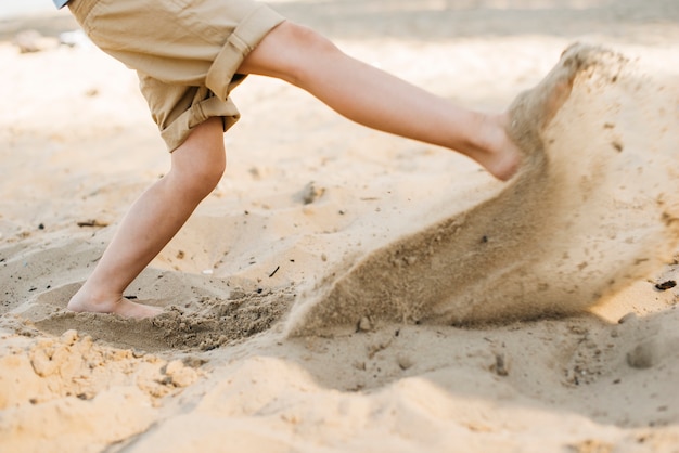 Ragazzo che dà dei calci alla sabbia alla spiaggia