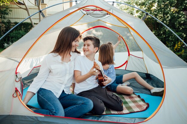 Ragazzo che esamina sua madre mentre giocando ukulele in tenda