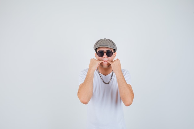 Ragazzo che fischia con le piccole dita in t-shirt, cappello e guardando sicuro di sé, vista frontale.