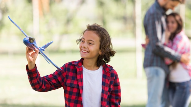 Ragazzo che gioca con l'aereo e genitori defocused al parco