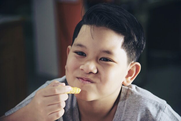 Ragazzo che mangia patatine fritte con salsa immersa sul tavolo di legno bianco