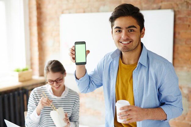 Ragazzo che mostra uno smartphone mentre si tiene una tazza di caffè e una ragazza che mangia con le bacchette