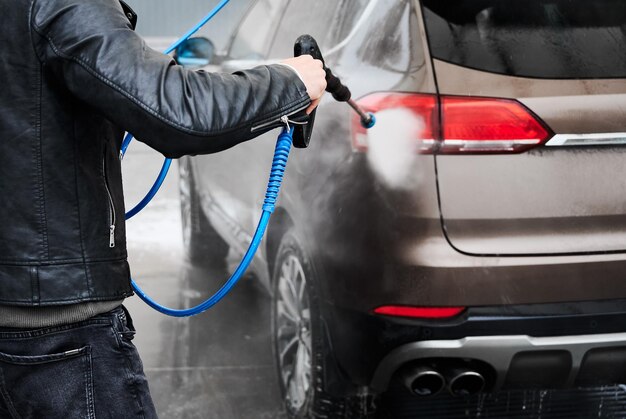 Ragazzo che risciacqua l'auto all'autolavaggio con una pistola ad acqua