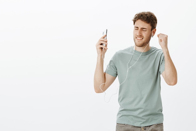 Ragazzo che sente una carica di energia grazie alla musica negli auricolari. Ritratto di piacere maschio bello rilassante ballare con gli occhi chiusi durante l'ascolto di canzoni in auricolari