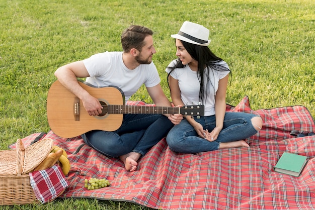 Ragazzo che suona la chitarra per la sua ragazza su una coperta da picnic