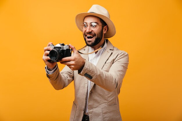 Ragazzo con cappello e giacca beige scatta foto con una fotocamera retrò su sfondo arancione