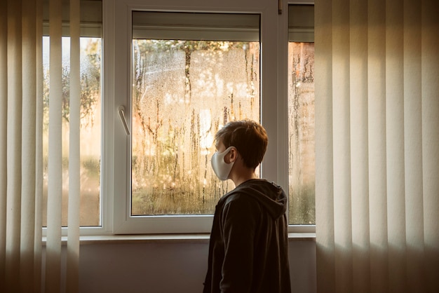 Ragazzo con la maschera per il viso in piedi accanto alle finestre