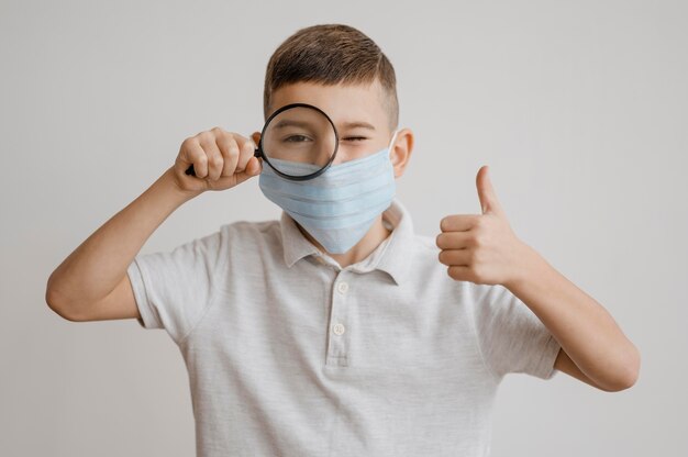 Ragazzo con mascherina medica utilizzando una lente d'ingrandimento in classe