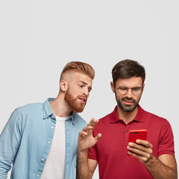 Ragazzo curioso con barba e taglio di capelli allo zenzero fa capolino nello smart phone del suo amico