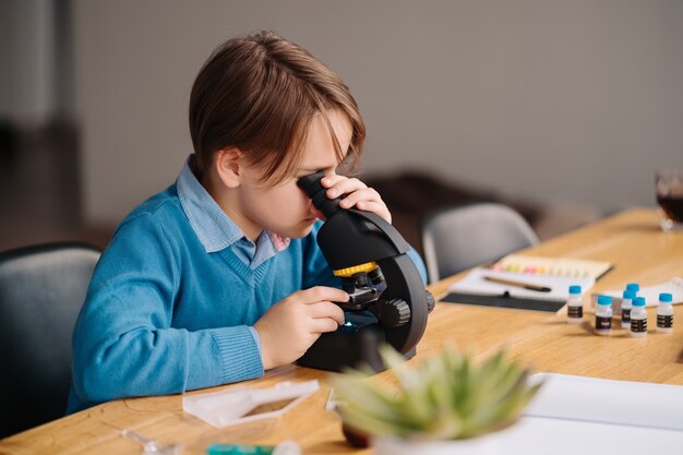 Ragazzo del primo grado che studia a casa usando il microscopio