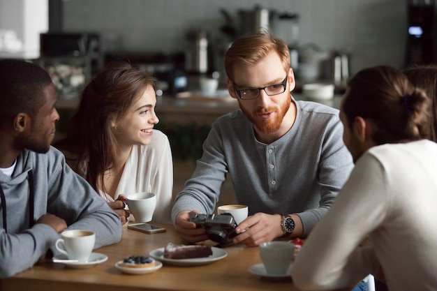 Ragazzo della testarossa che mostra le foto della macchina fotografica a diversi amici nella caffetteria