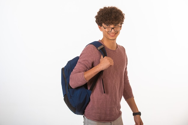 Ragazzo di capelli ricci in occhiali optique che tiene il suo zaino e sorridente.