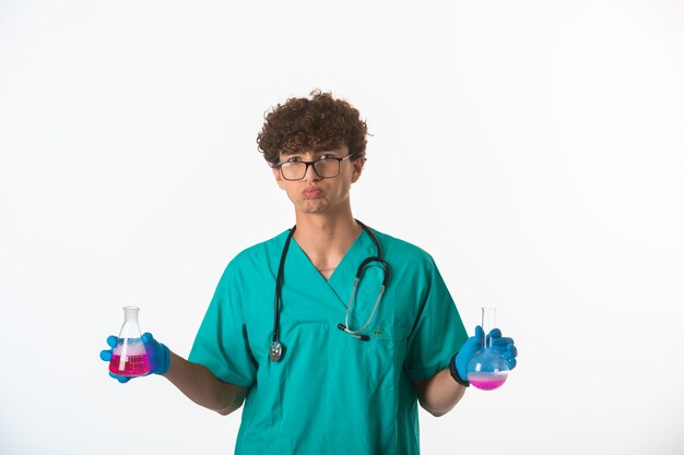 Ragazzo di capelli ricci in uniforme medica e maschere per le mani che fanno test e sembrano confusi.