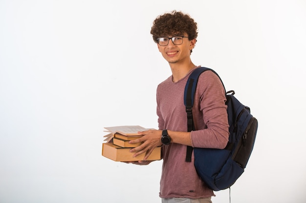 Ragazzo di capelli ricci in vetri optique che tengono i libri di scuola e che sorridono.