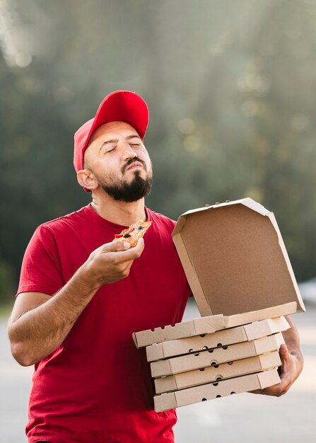 Ragazzo di consegna soddisfatto colpo medio che mangia pizza