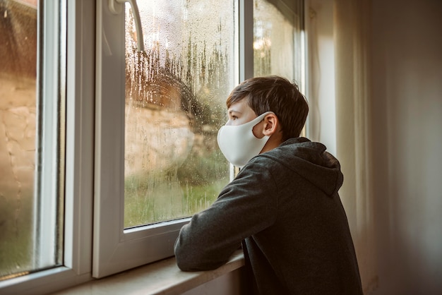 Ragazzo di lato con la maschera per il viso guardando attraverso la finestra