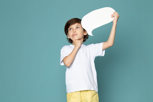 ragazzo di pensiero adorabile dolce carino in maglietta bianca che tiene insegna bianca sulla parete blu