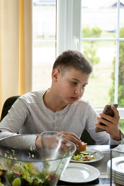 Ragazzo di tiro medio che mangia con lo smartphone