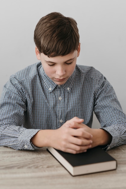 Ragazzo di vista frontale che prega con le sue mani su un libro sacro