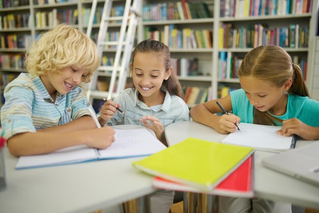 Ragazzo e due ragazze che scrivono e dipingono in biblioteca