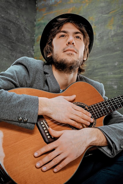 Ragazzo figo con cappello seduto con la chitarra