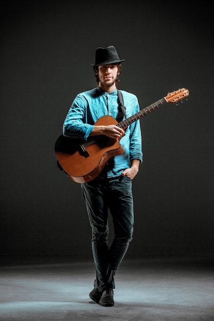 Ragazzo freddo in piedi con la chitarra su sfondo scuro