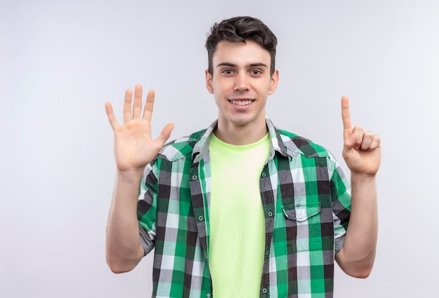 Ragazzo giovane caucasico sorridente che indossa la camicia verde che mostra cinque e uno con le mani su fondo bianco isolato