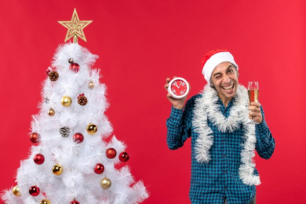 Ragazzo giovane emotivo pazzo con cappello di Babbo Natale e in possesso di un bicchiere di vino e orologio in piedi