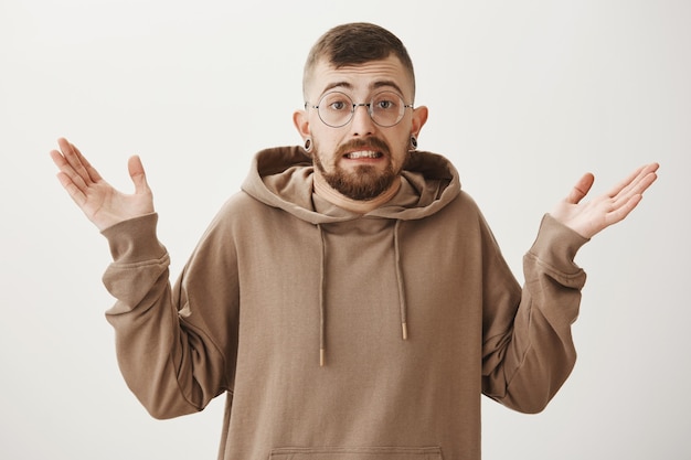 Ragazzo hipster impacciato colpevole con gli occhiali allargò le mani senza tracce e alzando le spalle