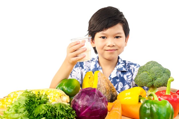Ragazzo in buona salute asiatico che mostra espressione felice con un bicchiere di latte e varietà di verdure fresche