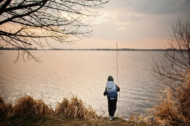 Ragazzo in felpa con cappuccio in riva al lago con una canna in mano