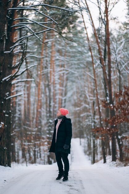 Ragazzo in piedi sulla strada in mezzo alla foresta circondata dalla neve