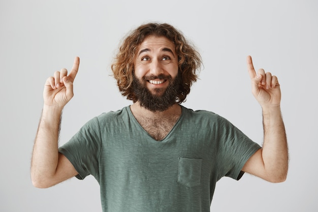 Ragazzo mediorientale sorridente allegro con la barba che osserva e che indica le barrette in su