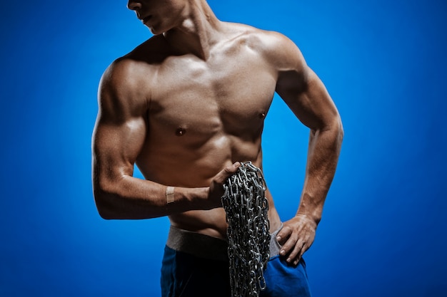 Ragazzo muscoloso con catene sulle spalle contro un muro blu