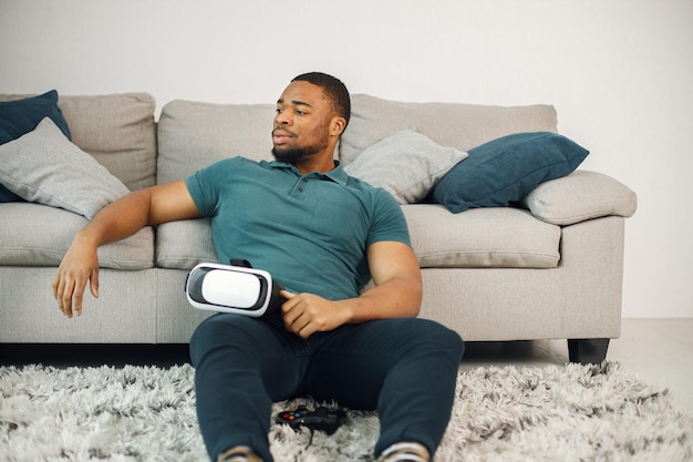 Ragazzo nero con occhiali per realtà virtuale seduto su un tappeto in soggiorno