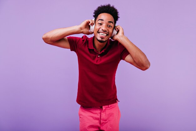 Ragazzo nero emozionante con sorridente acconciatura divertente. Tiro al coperto di ridere uomo gioioso in camicia rossa.