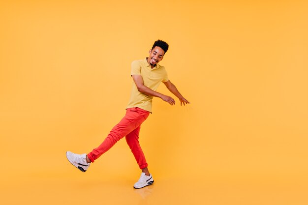 Ragazzo nero ispirato in abiti casual luminosi e divertenti. Modello maschio africano di risata in maglietta gialla e pantaloni rossi che scherzano.