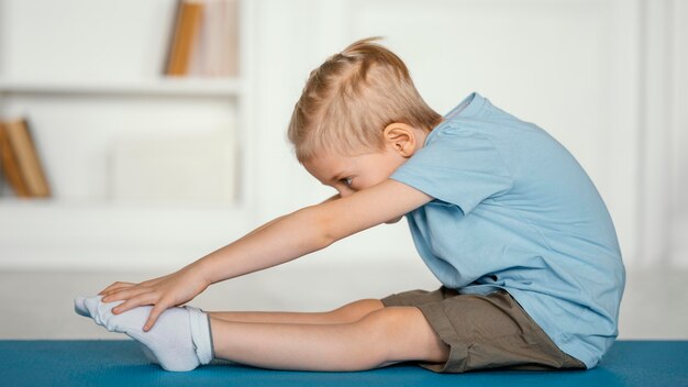 Ragazzo pieno del colpo che allunga sulla stuoia di yoga