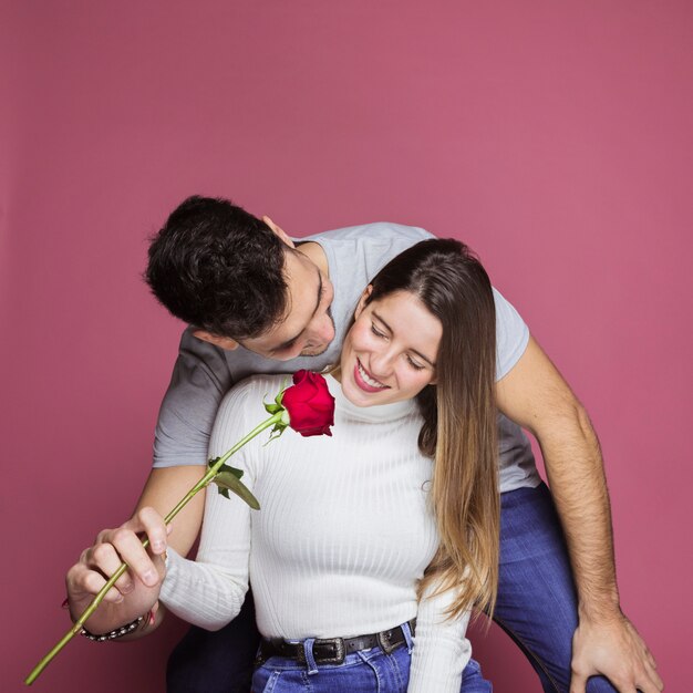 Ragazzo positivo che presenta rosa fresca ad attraente signora allegra