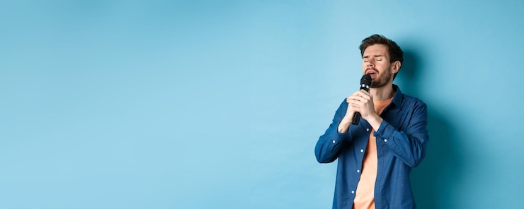 Foto gratuito ragazzo romantico che canta nel microfono esibendosi sul palco in piedi su sfondo blu