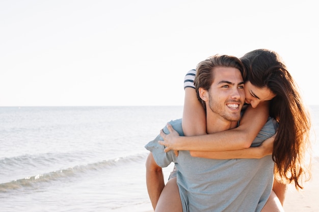 Ragazzo sorridente che trasportano fidanzata in spiaggia