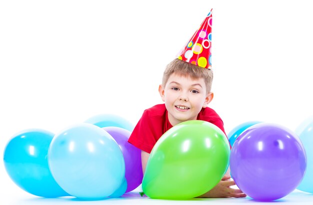 Ragazzo sorridente felice in maglietta rossa sdraiato sul pavimento con palloncini colorati - isolato su un bianco