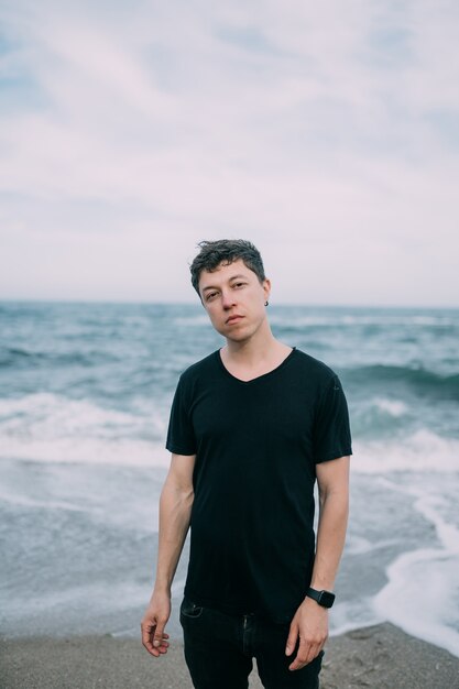 Ragazzo sorridente in una maglietta nera si trova sulla spiaggia sabbiosa.