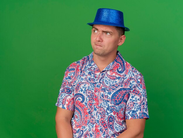 Ragazzo sospettoso giovane partito che indossa cappello blu isolato sul verde