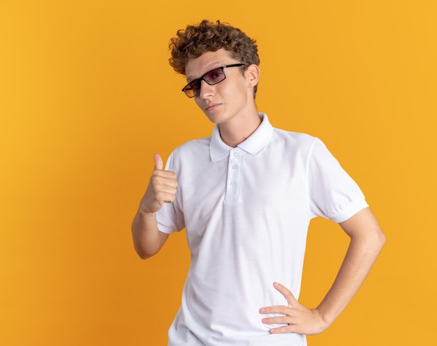 Ragazzo studente in abbigliamento casual con gli occhiali che mostra il pollice in alto sorridente