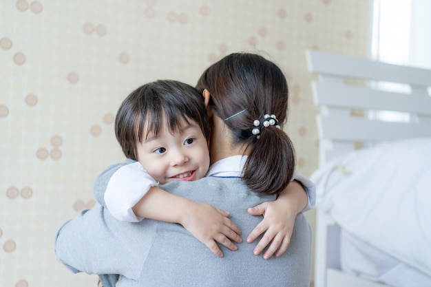 Ragazzo sveglio asiatico che sorride con felicemente e che abbraccia con la madre a casa, spazio della copia, concetto "nucleo familiare"