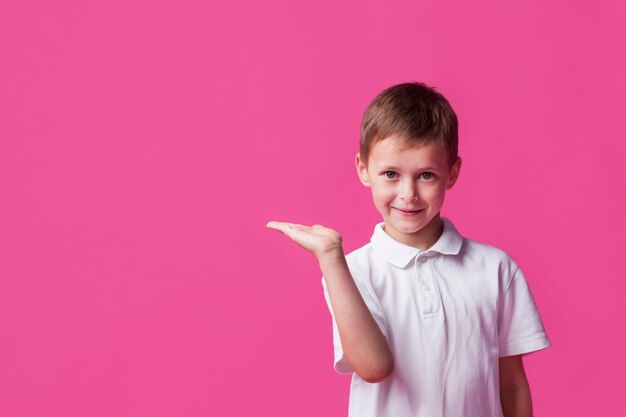 Ragazzo sveglio sorridente che presenta sul contesto rosa