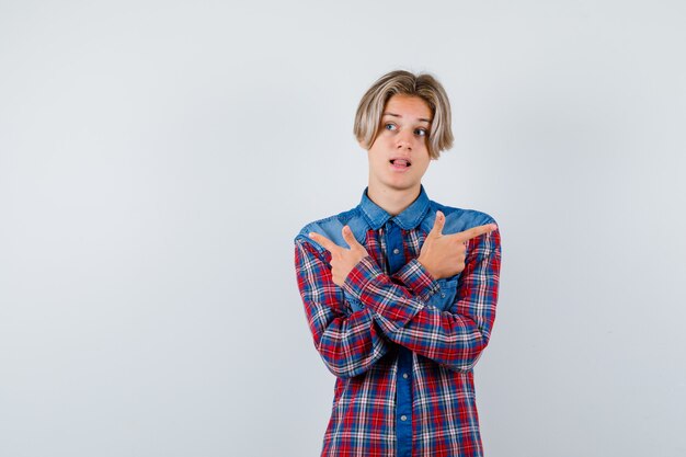 Ragazzo teenager che indica entrambi i lati in camicia a quadretti e che sembra divertente, vista frontale.